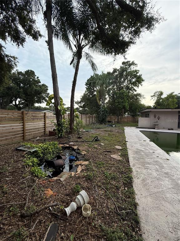 A backyard features a small pond, a wooden fence, and large trees with climbing plants — 384 LENTZ ROAD, BELLEAIR BLUFFS, FL