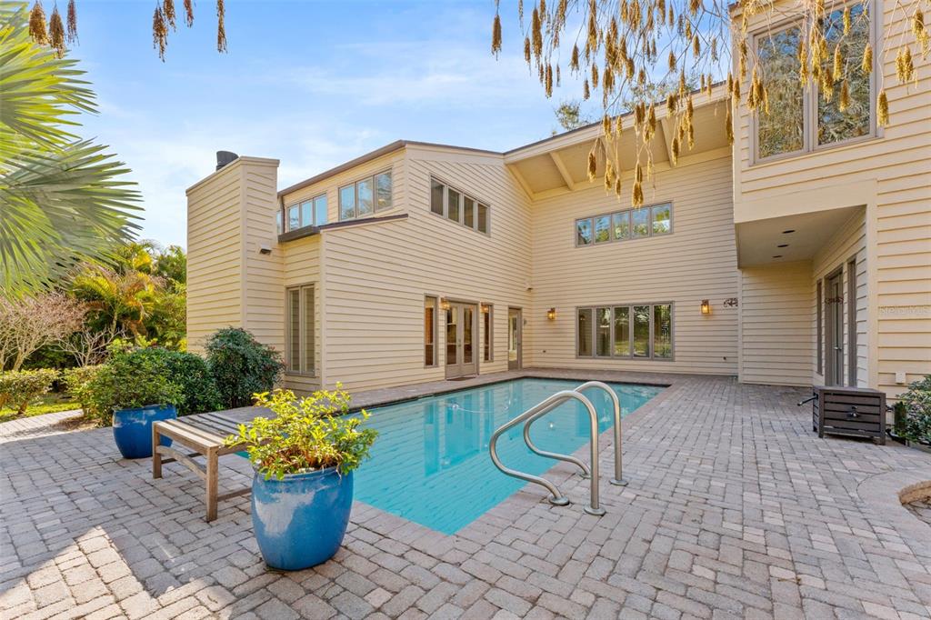A two-story house with light siding overlooks a rectangular swimming pool on a brick patio — 1351 WILLOW BROOK DR, PALM HARBOR, FL