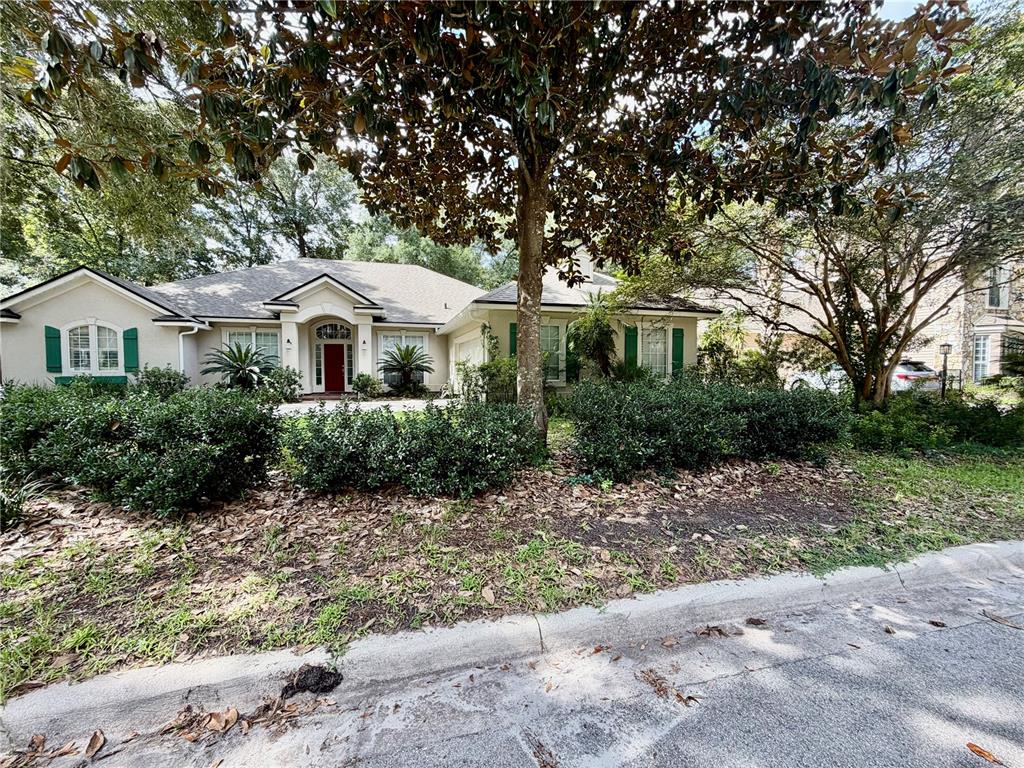 A single-story house with a red front door, green shutters, and a large magnolia tree — 9717 SW 32ND LANE, GAINESVILLE, FL