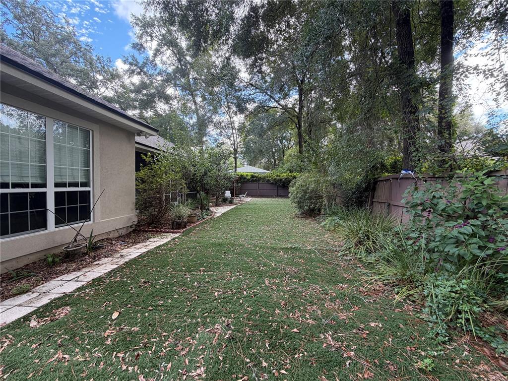A grassy backyard features a stone walkway, mature trees, and a wooden privacy fence — 9717 SW 32ND LANE, GAINESVILLE, FL