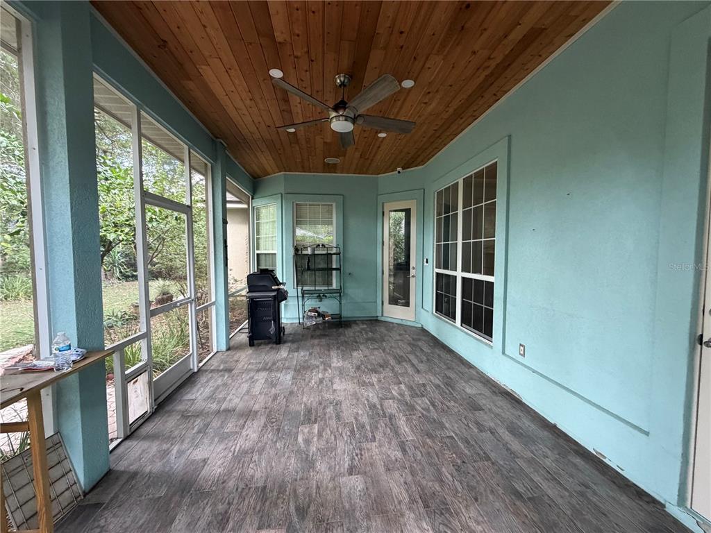 A screened-in porch features a wood-paneled ceiling, a ceiling fan, and gray wood-look flooring — 9717 SW 32ND LANE, GAINESVILLE, FL
