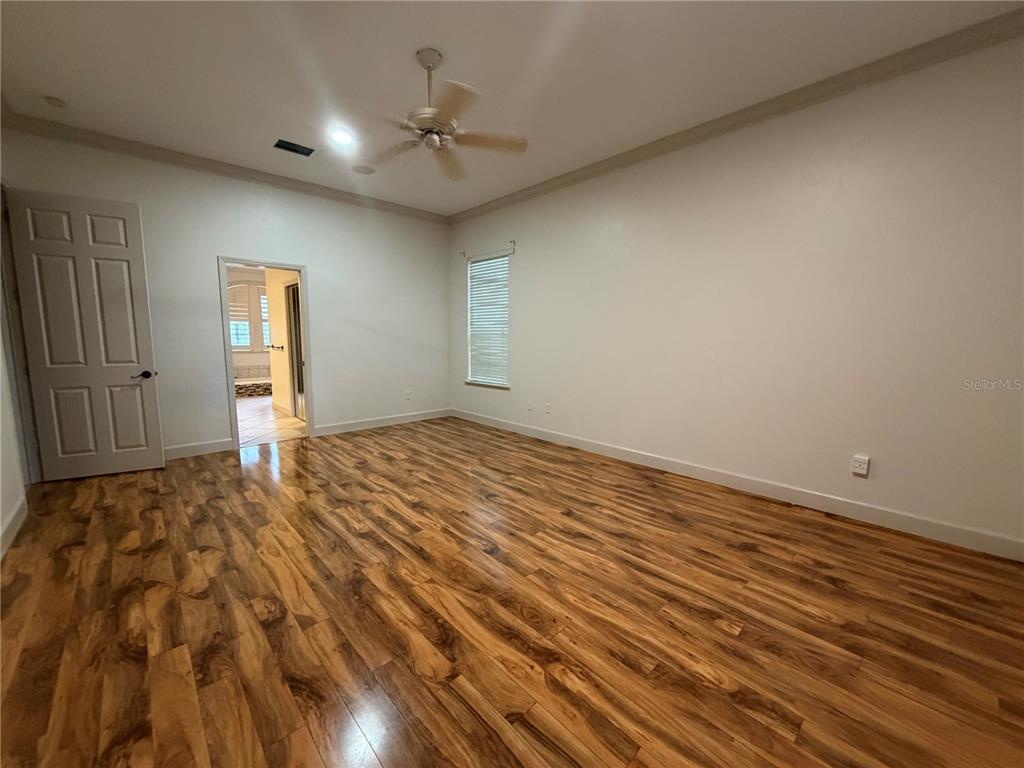 An empty bedroom features light-colored walls, crown molding, a ceiling fan, and wood-look flooring — 9717 SW 32ND LANE, GAINESVILLE, FL