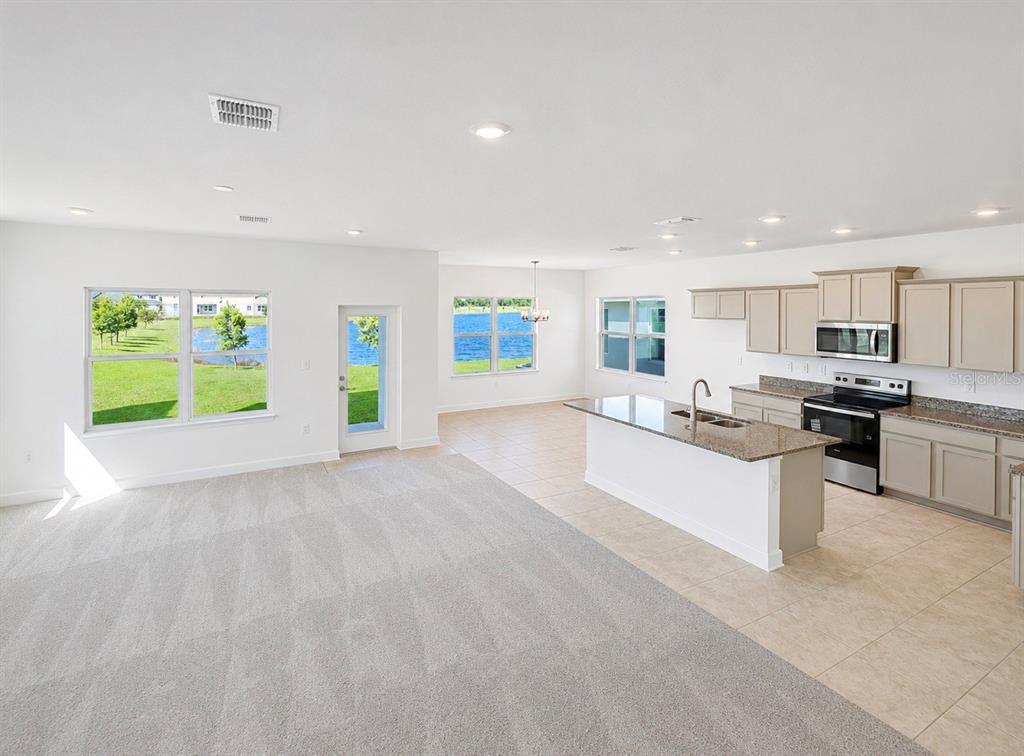 An open-concept kitchen and living area features light-colored cabinetry, granite countertops, and carpeted flooring — 7575 BENT TREE LOOP, HARMONY, FL