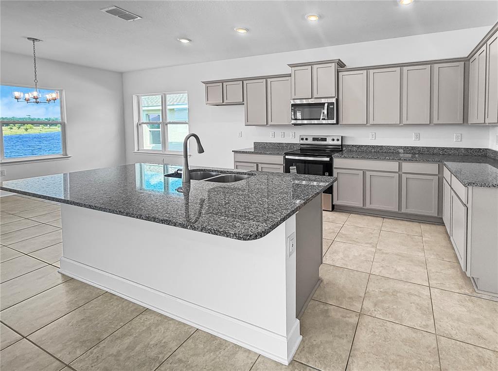 A kitchen features gray cabinets, granite countertops, a central island, and a view of water — 7575 BENT TREE LOOP, HARMONY, FL