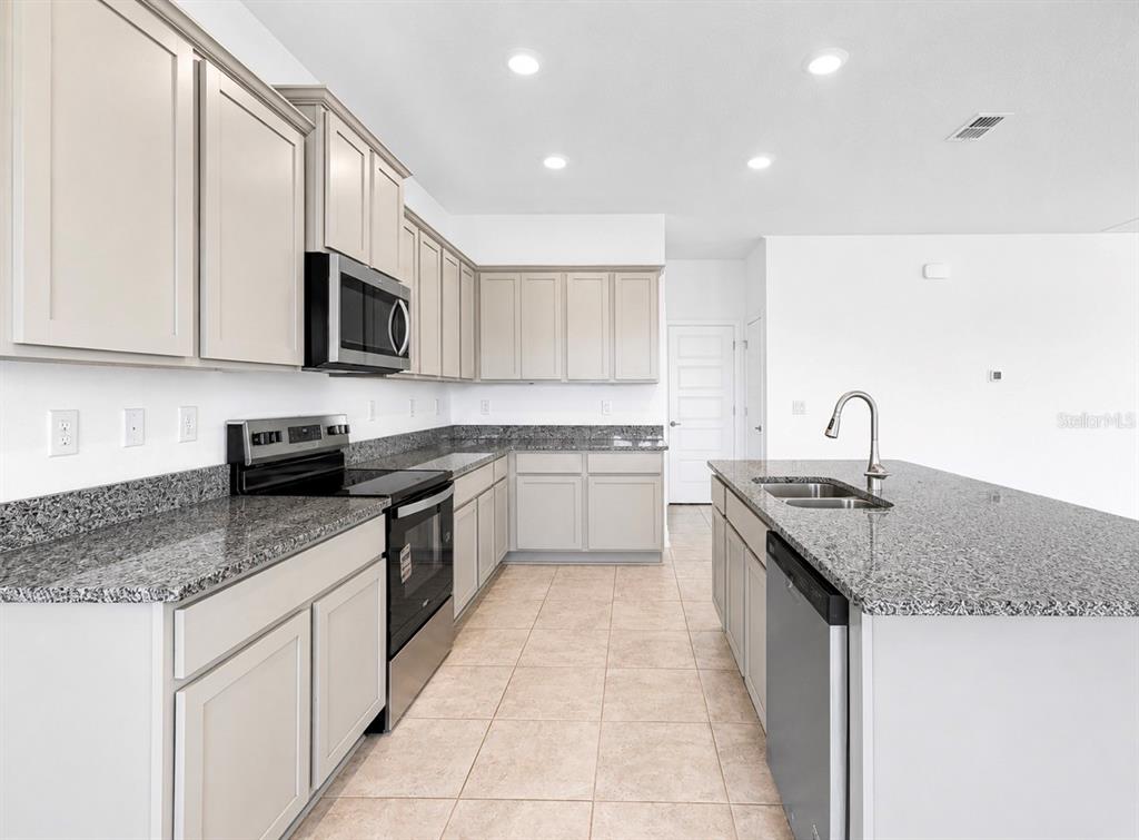 A kitchen features light gray cabinets, granite countertops, stainless steel appliances, and a center island — 7575 BENT TREE LOOP, HARMONY, FL
