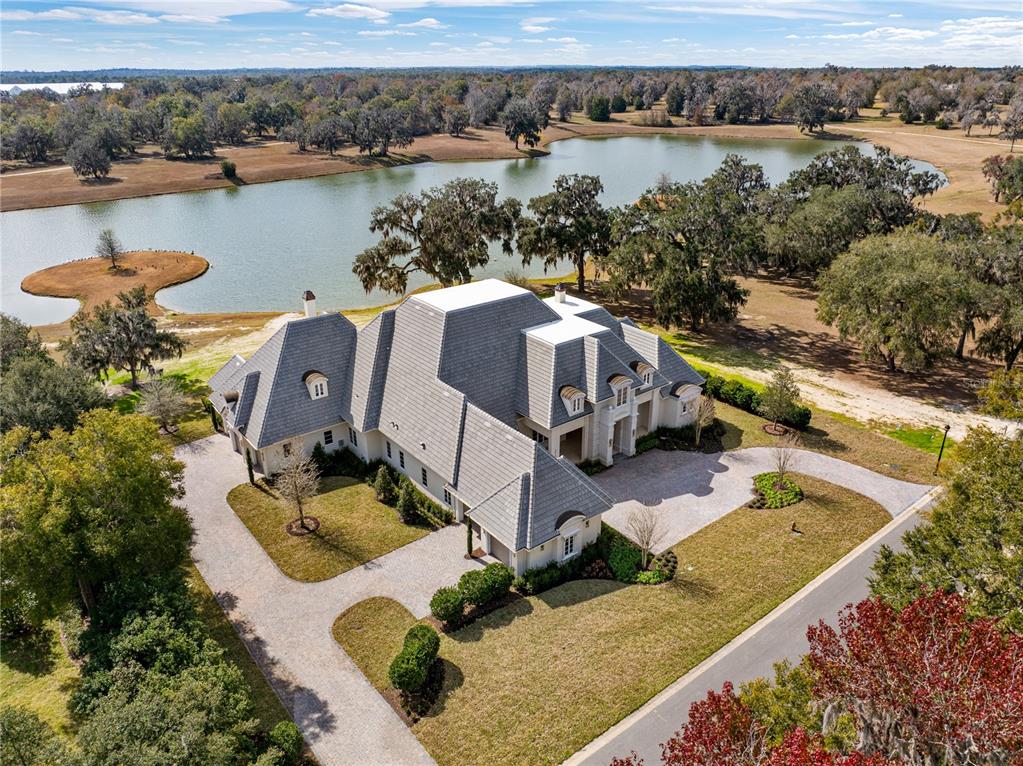 An aerial view of a large house with a gray roof situated beside a lake — 8570 NW 31ST LANE ROAD, OCALA, FL
