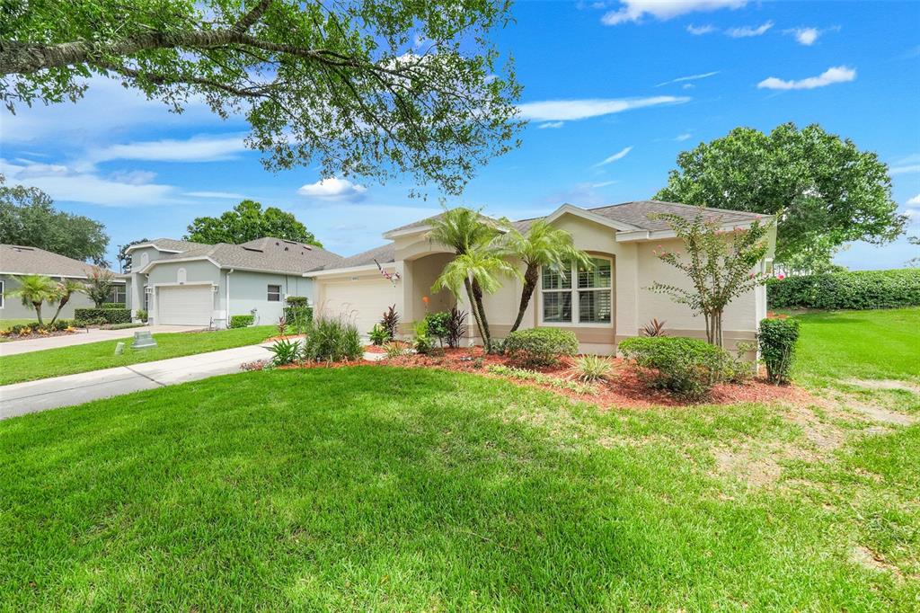 A single-story beige house with a two-car garage, palm trees, and a manicured lawn — 2525 NEW CASTLE COURT, CLERMONT, FL