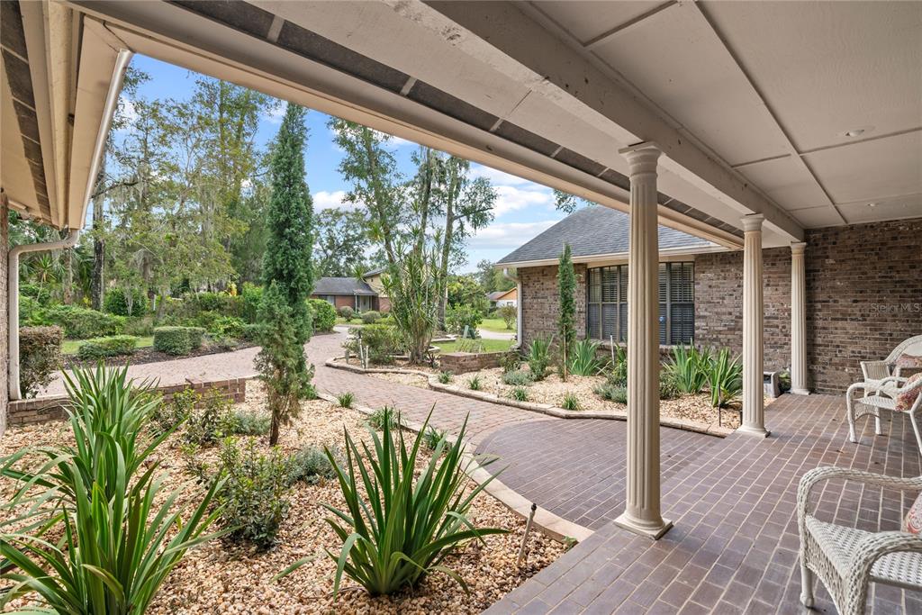 A covered brick porch overlooks a landscaped yard with a brick walkway and mature trees — 1111 AUDUBON WAY, MAITLAND, FL