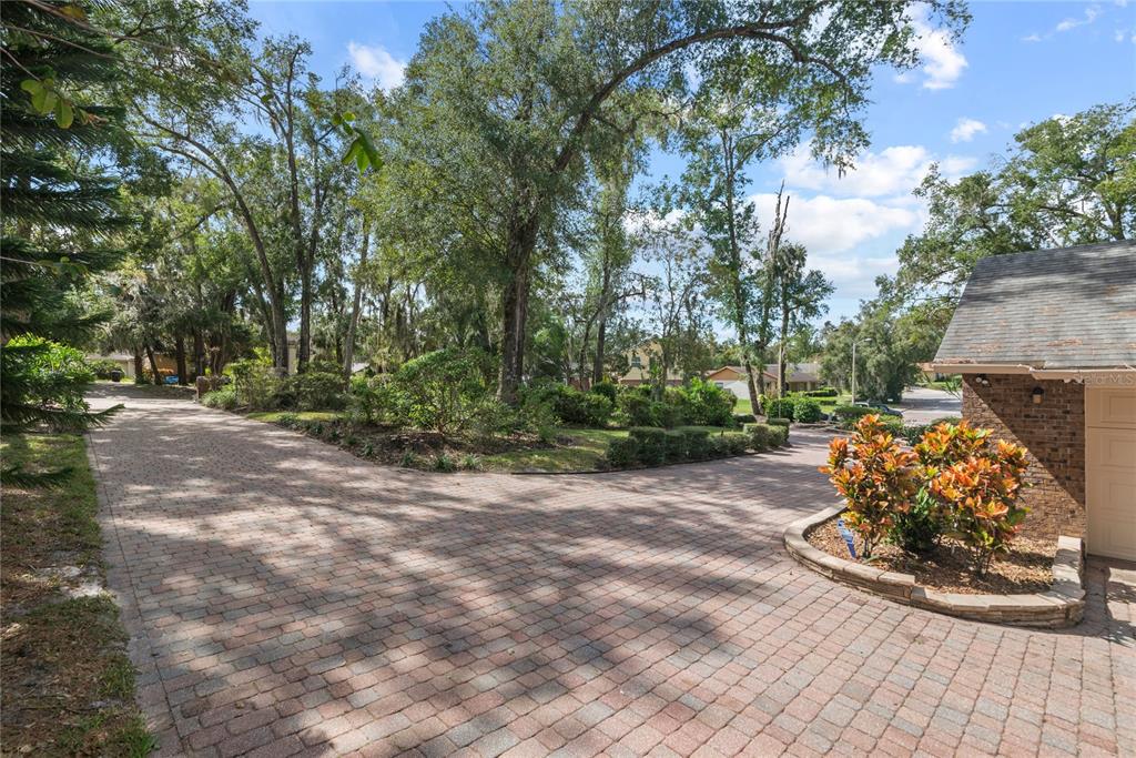 A paved driveway leads toward a brick house exterior surrounded by mature trees and landscaping — 1111 AUDUBON WAY, MAITLAND, FL