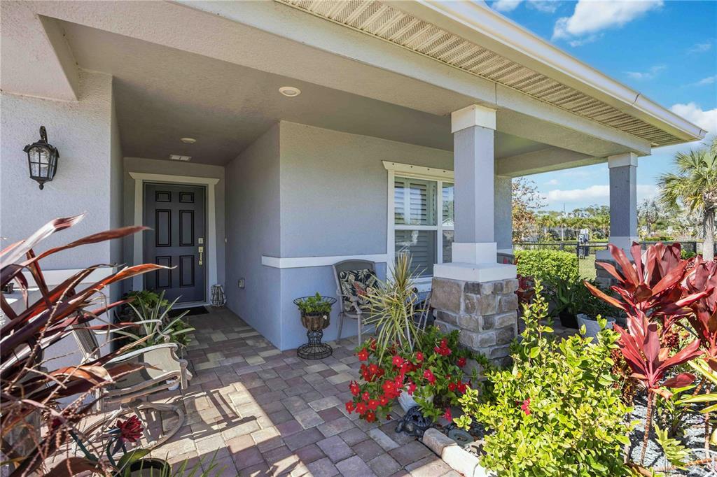 A covered front porch features a paved floor, stone-based columns, and a dark gray front door — 3576 74TH AVENUE CIRCLE E, SARASOTA, FL