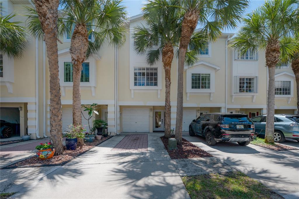 A row of three-story townhomes with light yellow siding, white trim, and attached garages — 119 BRENT CIRCLE, OLDSMAR, FL