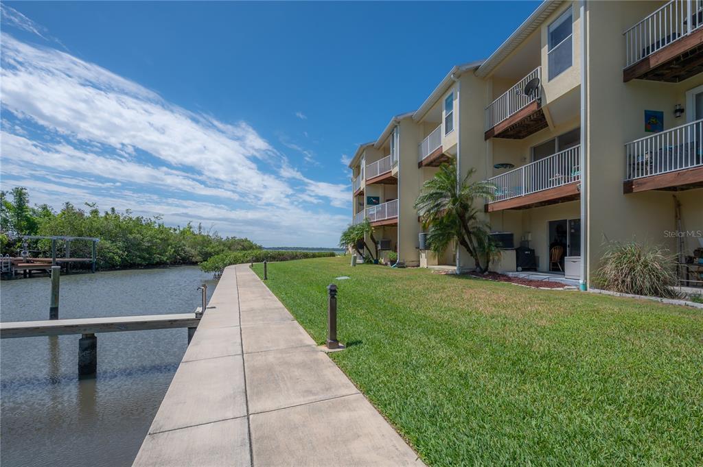 A concrete walkway runs alongside a grassy lawn and a multi-story apartment building by water — 119 BRENT CIRCLE, OLDSMAR, FL