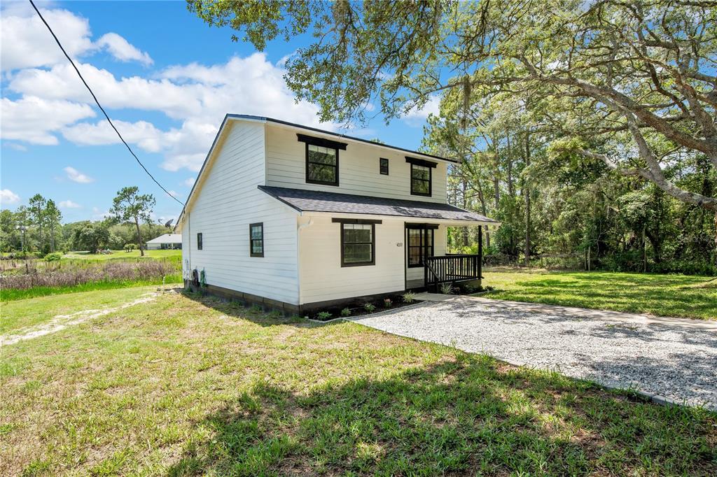 A two-story white house with black trim sits on a gravel driveway near trees — 42111 CHINABERRY COURT, EUSTIS, FL
