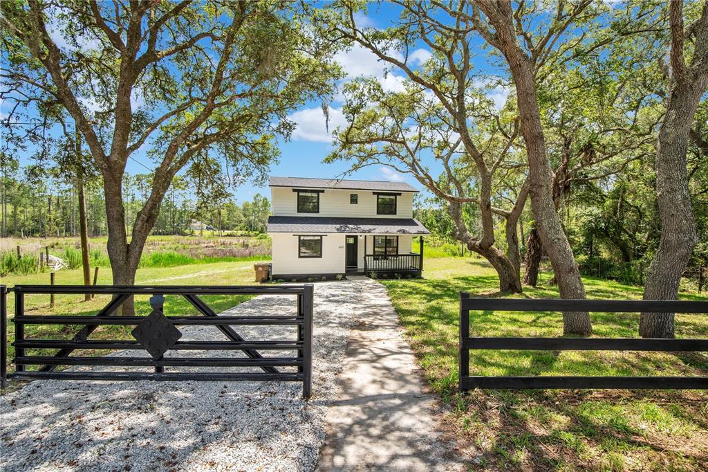 A two-story white house with black trim sits behind a black fence and gravel driveway — 42111 CHINABERRY COURT, EUSTIS, FL
