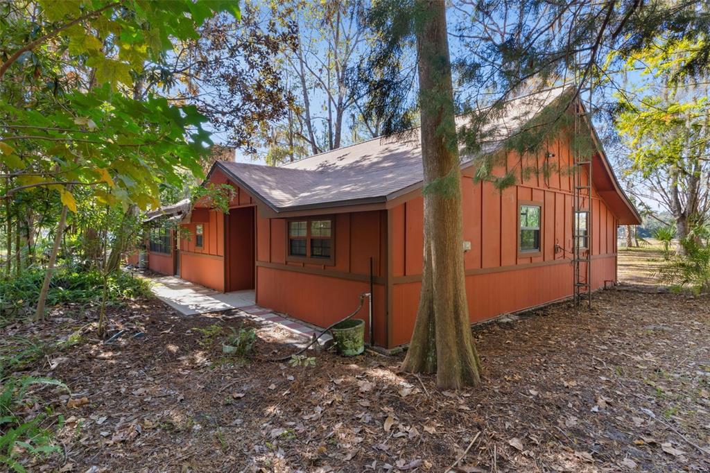 A single-story house with orange board-and-batten siding sits in a wooded, leaf-covered yard — 6250 & 5942 E C 478, CENTER HILL, FL