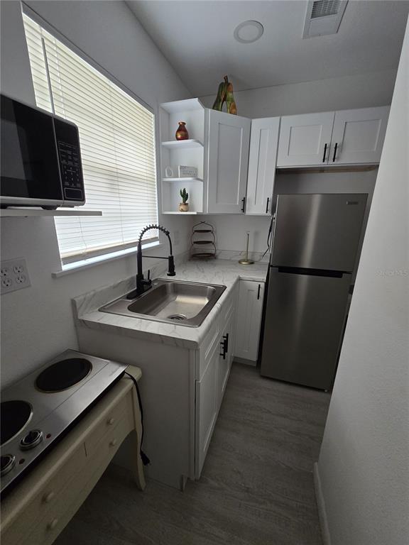 A small kitchen features white cabinets, a stainless steel refrigerator, and a marble-patterned countertop — 1190 PECAN STREET, KISSIMMEE, FL