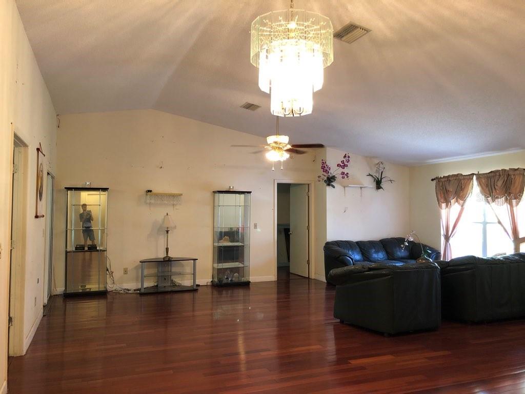 A living room with hardwood floors, a large chandelier, and a dark leather sofa set — 11716 CR 672 HIGHWAY, RIVERVIEW, FL