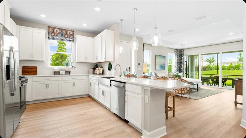A white kitchen with a center island and stainless steel appliances opens to a living area — 7516 MOONBEAM AVENUE, SARASOTA, FL