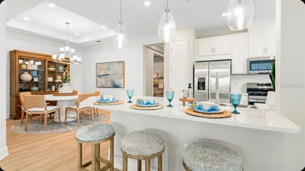 A kitchen with a white quartz island and bar stools next to a dining area — 7516 MOONBEAM AVENUE, SARASOTA, FL