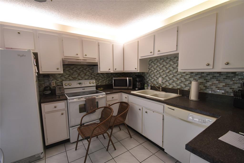 A kitchen with white cabinets, dark countertops, a tiled backsplash, and two wicker chairs — 1709 CLOWER CREEK DRIVE UNIT BR 104, SARASOTA, FL