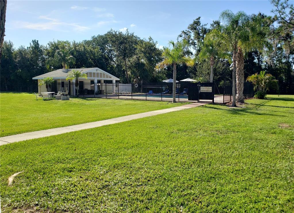 A community swimming pool area with a clubhouse, palm trees, and a surrounding black fence — 22706 GAGE LOOP UNIT 33, LAND O LAKES, FL