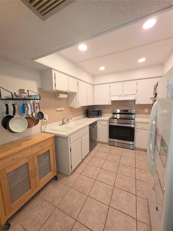 A kitchen features white cabinets, stainless steel appliances, tile flooring, and a wooden rolling cart — 2101 SUNSET POINT ROAD UNIT 2603, CLEARWATER, FL