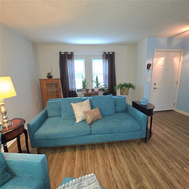 A living room features a blue sofa, wood-look flooring, and a front door — 2101 SUNSET POINT ROAD UNIT 2603, CLEARWATER, FL