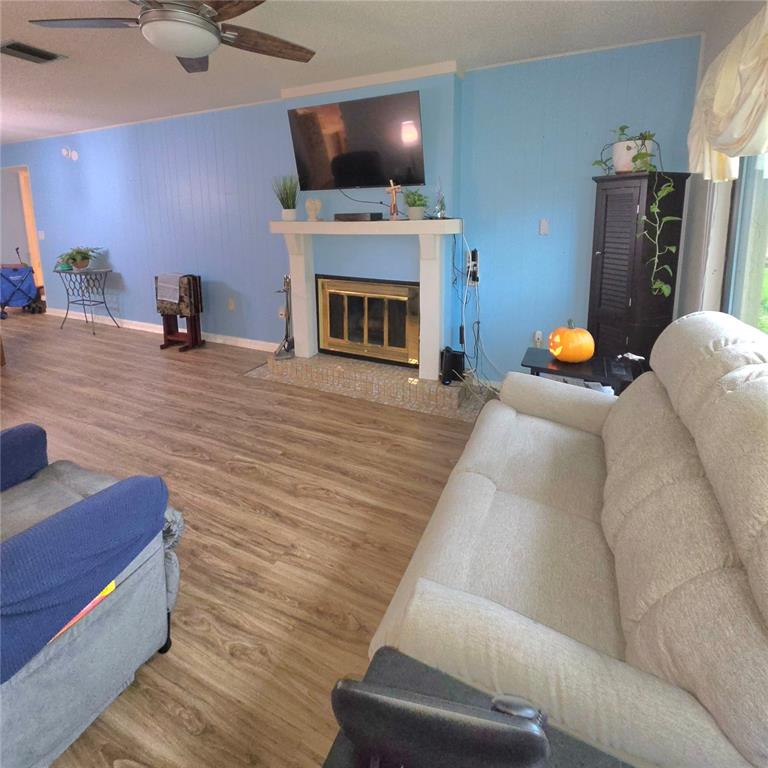 A living room features light blue walls, wood-look flooring, a fireplace, and a beige sofa — 2101 SUNSET POINT ROAD UNIT 2603, CLEARWATER, FL