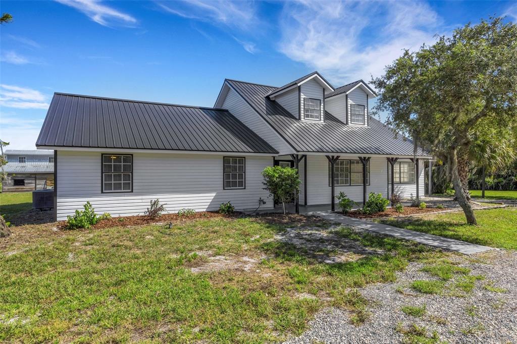 A white house with a black metal roof and two dormer windows sits on grass — 28706 102ND DRIVE E, MYAKKA CITY, FL