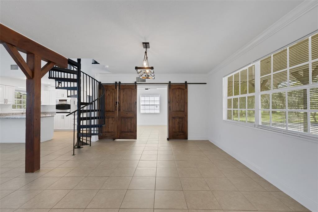 A room with tile flooring, a black spiral staircase, and wooden sliding barn doors — 28706 102ND DRIVE E, MYAKKA CITY, FL