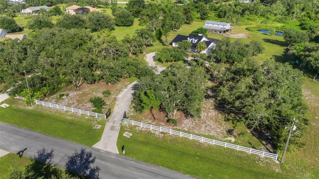 An aerial view shows a house with a white fence, driveway, and trees on land — 28706 102ND DRIVE E, MYAKKA CITY, FL