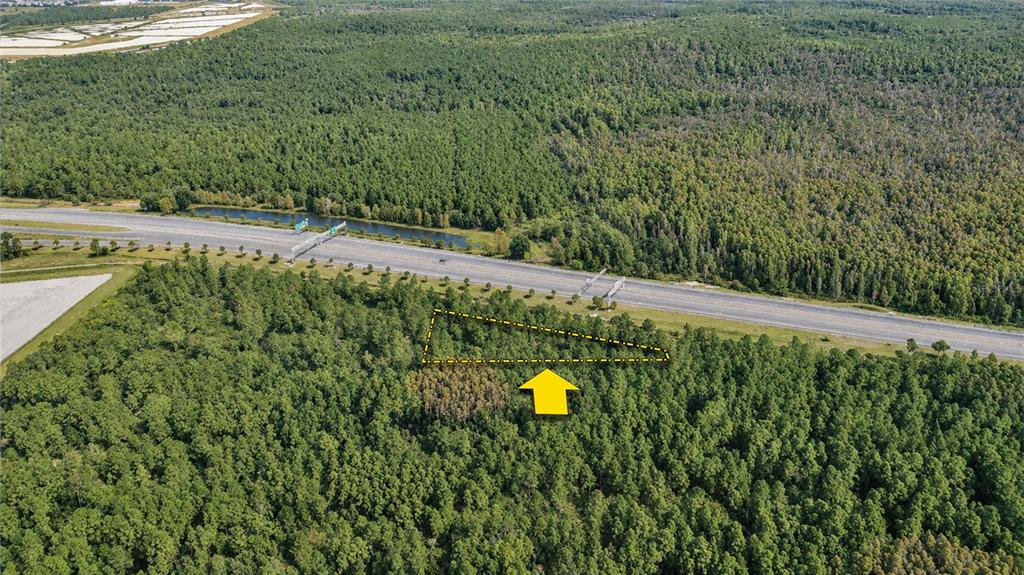An aerial view shows a wooded lot marked by a yellow outline near a highway — Vacant Land on S APOPKA VINELAND ROAD, ORLANDO, FL