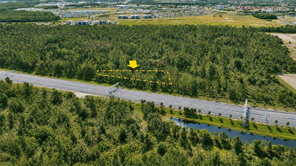 An aerial view shows a wooded lot outlined in yellow adjacent to a multi-lane highway — Vacant Land on S APOPKA VINELAND ROAD, ORLANDO, FL
