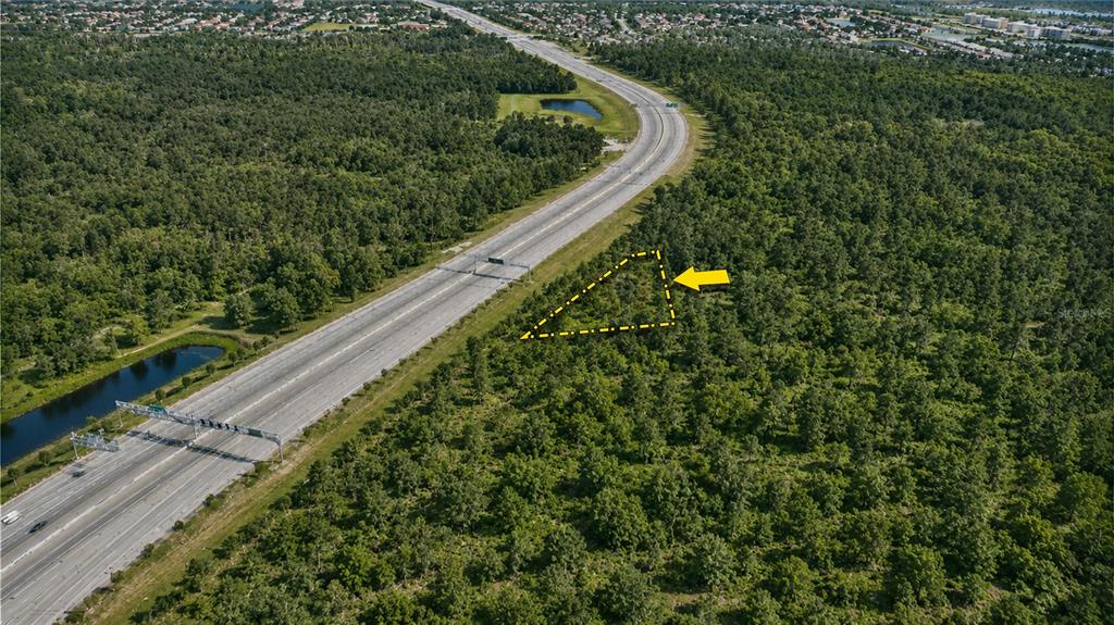 An aerial view shows a triangular plot of land adjacent to a multi-lane highway — Vacant Land on S APOPKA VINELAND ROAD, ORLANDO, FL