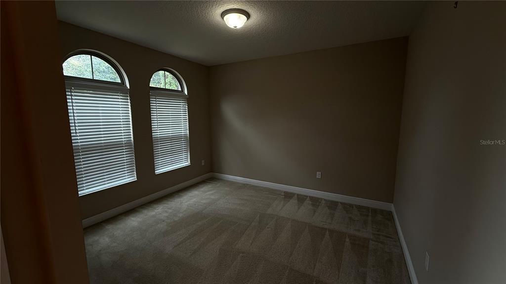 An empty bedroom features beige walls, carpeted flooring, and two arched windows with blinds — 109 VERDE WAY, DEBARY, FL