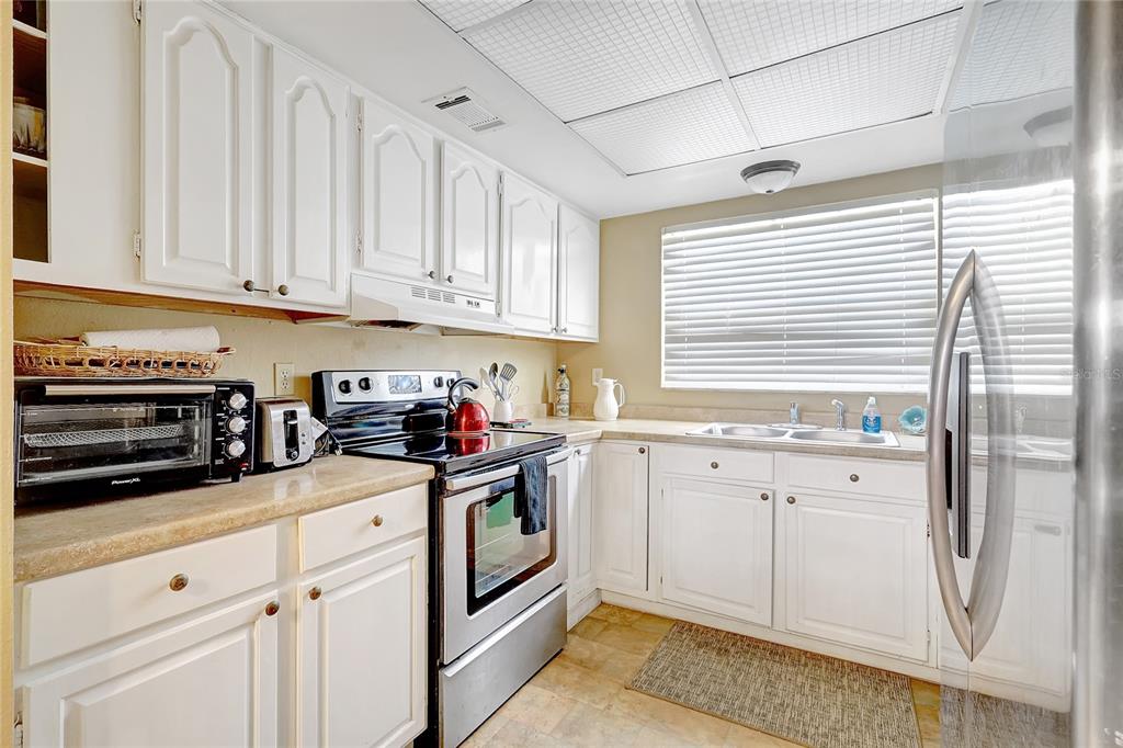 A kitchen features white cabinets, stainless steel appliances, a double sink, and a window with blinds — 2811 S PINES DRIVE UNIT 15, LARGO, FL