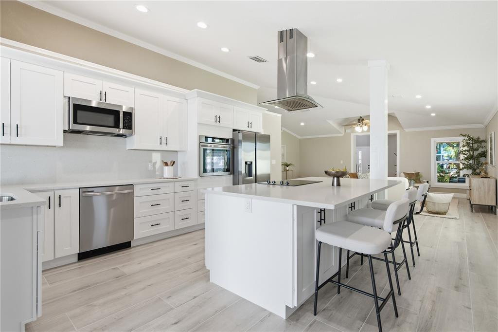 A modern kitchen features white cabinets, stainless steel appliances, a large island, and light flooring — 302 SHORE DRIVE, PALM HARBOR, FL