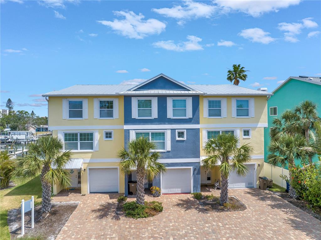 A three-story, multi-unit residential building features yellow and blue siding with a paved driveway — 100 WINDRUSH BOULEVARD UNIT 1, INDIAN ROCKS BEACH, FL