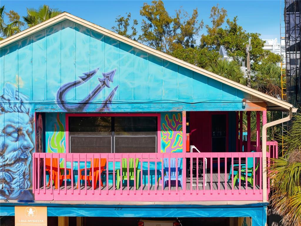 An elevated house exterior features a bright blue mural with a trident and pink balcony railing — 527 BEACH ROAD, SARASOTA, FL