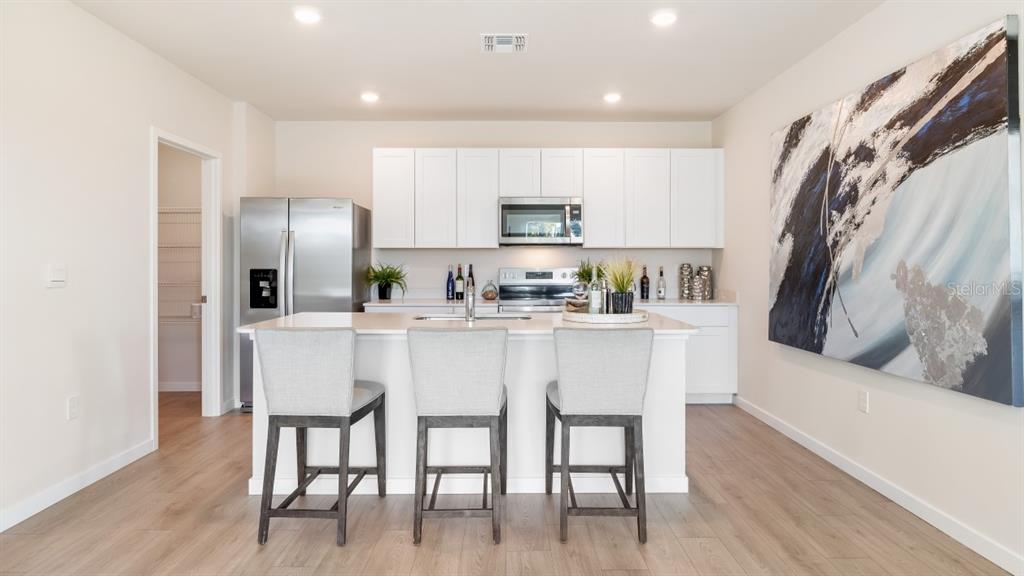 A modern kitchen features white cabinetry, stainless steel appliances, a central island, and bar seating — 4607 SCHUBERT TRAIL, NORTH PORT, FL