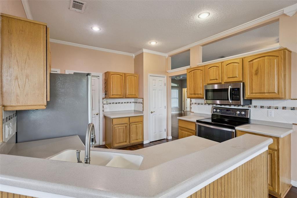 A kitchen features oak cabinets, light countertops, stainless steel appliances, and a breakfast bar — 15734 THOROUGHBRED LANE, MONTVERDE, FL