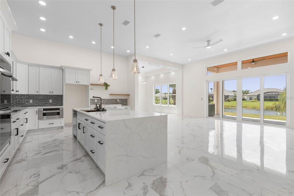 A modern kitchen with white cabinetry, a large marble island, and sliding glass doors — 116 LONGVIEW WAY N, PALM COAST, FL