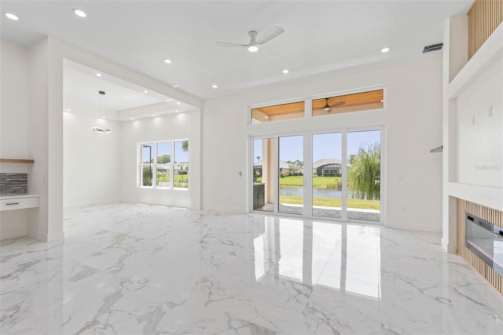 A bright living room features white marble floors, a fireplace, and sliding doors overlooking water — 116 LONGVIEW WAY N, PALM COAST, FL