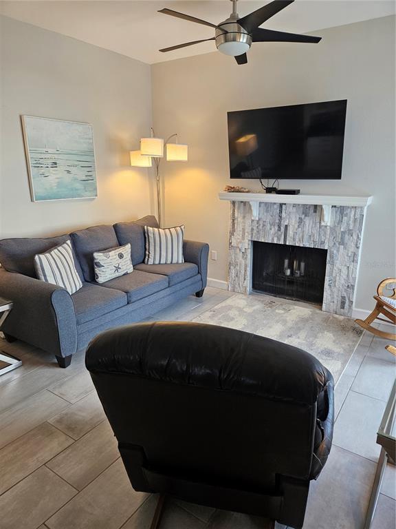 A living room features a gray sofa, a fireplace with stone surround, and a ceiling fan — 179 MEDALLION BOULEVARD UNIT E, MADEIRA BEACH, FL