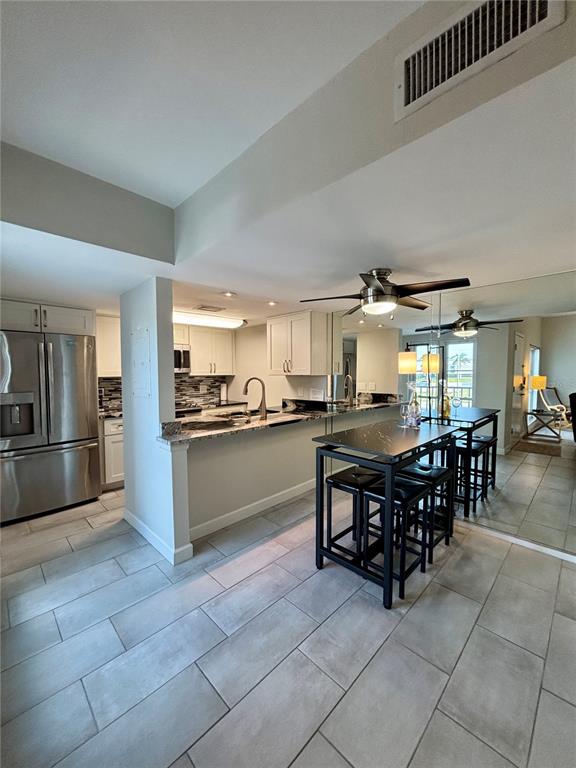 A kitchen with stainless steel appliances, white cabinets, and a dining table with stools — 179 MEDALLION BOULEVARD UNIT E, MADEIRA BEACH, FL