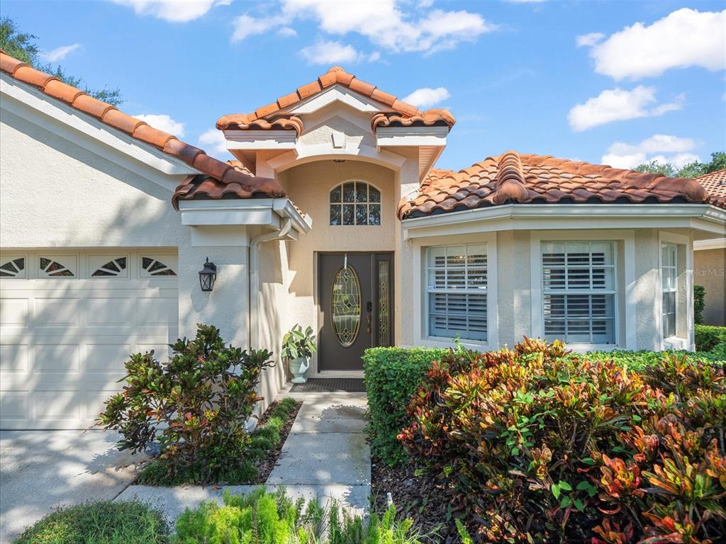A single-story house exterior features a tile roof, a garage, and a front entryway — 18921 PLACE MARQUETTE, LUTZ, FL