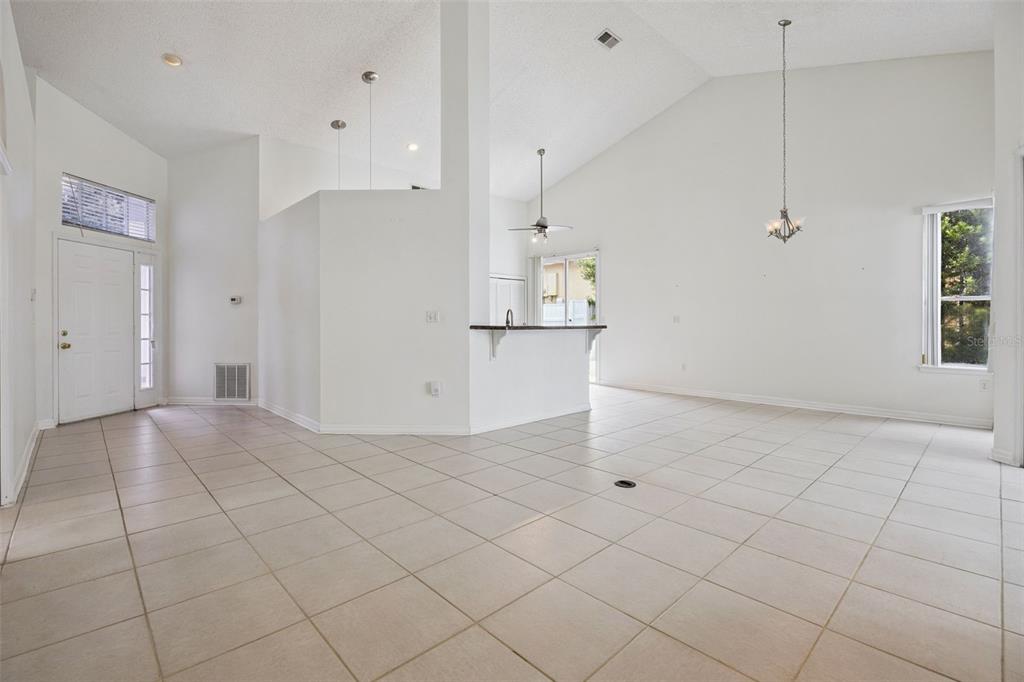An open-concept living area with white walls, vaulted ceilings, and light-colored tile flooring — 3774 HUNTWICKE BLVD, DAVENPORT, FL