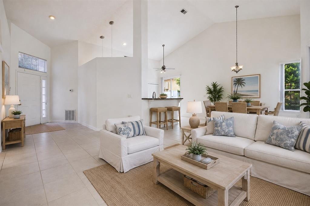 A bright, open-concept living and dining area with vaulted ceilings, tile floors, and neutral furniture — 3774 HUNTWICKE BLVD, DAVENPORT, FL