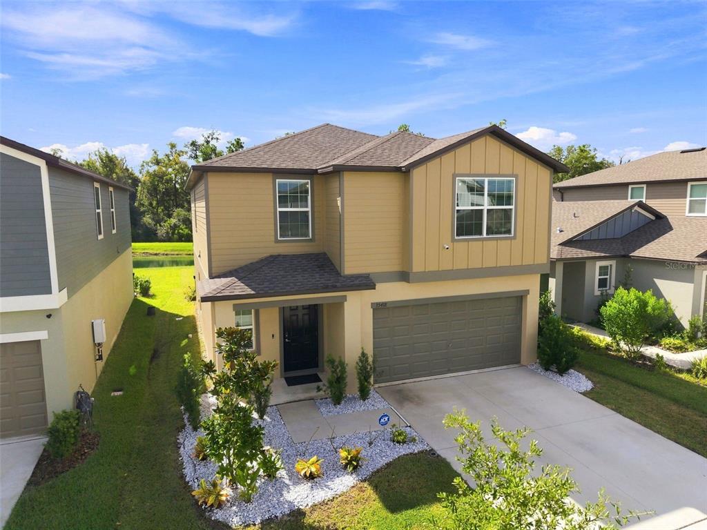 An exterior view of a two-story house with tan siding, a garage, and a landscaped yard — 35418 ACKLEY TRACE, ZEPHYRHILLS, FL