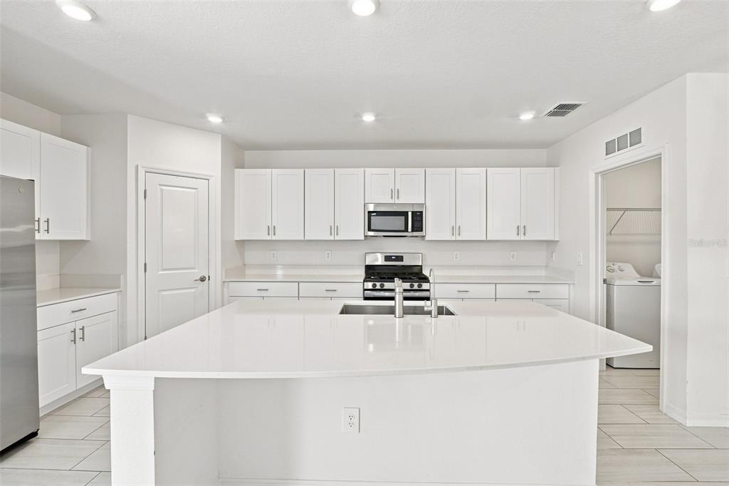 An open-concept kitchen and dining area features white cabinetry, a kitchen island, and tile flooring — 35418 ACKLEY TRACE, ZEPHYRHILLS, FL